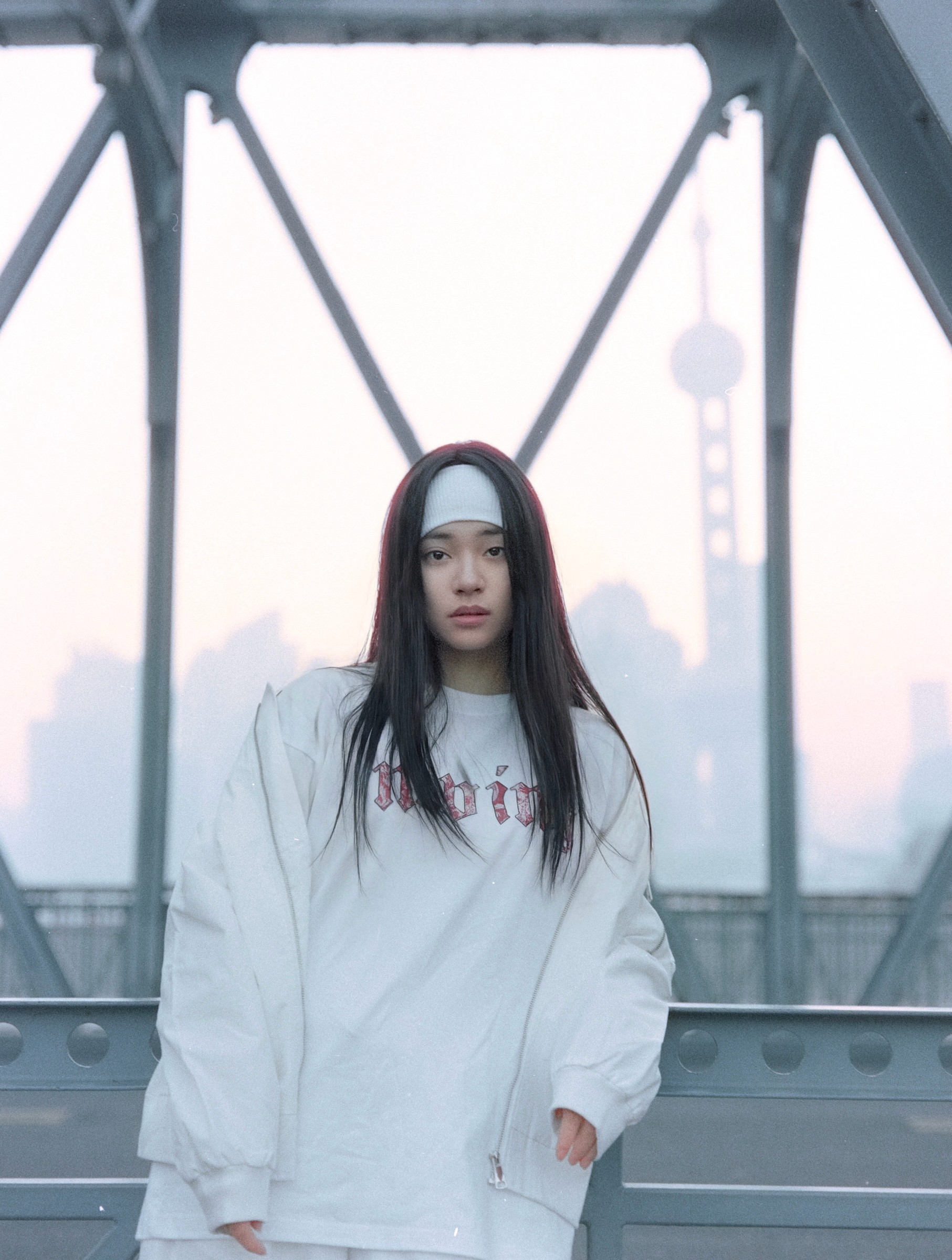Woman in an oversized white sweatshirt standing on a pedestrian bridge