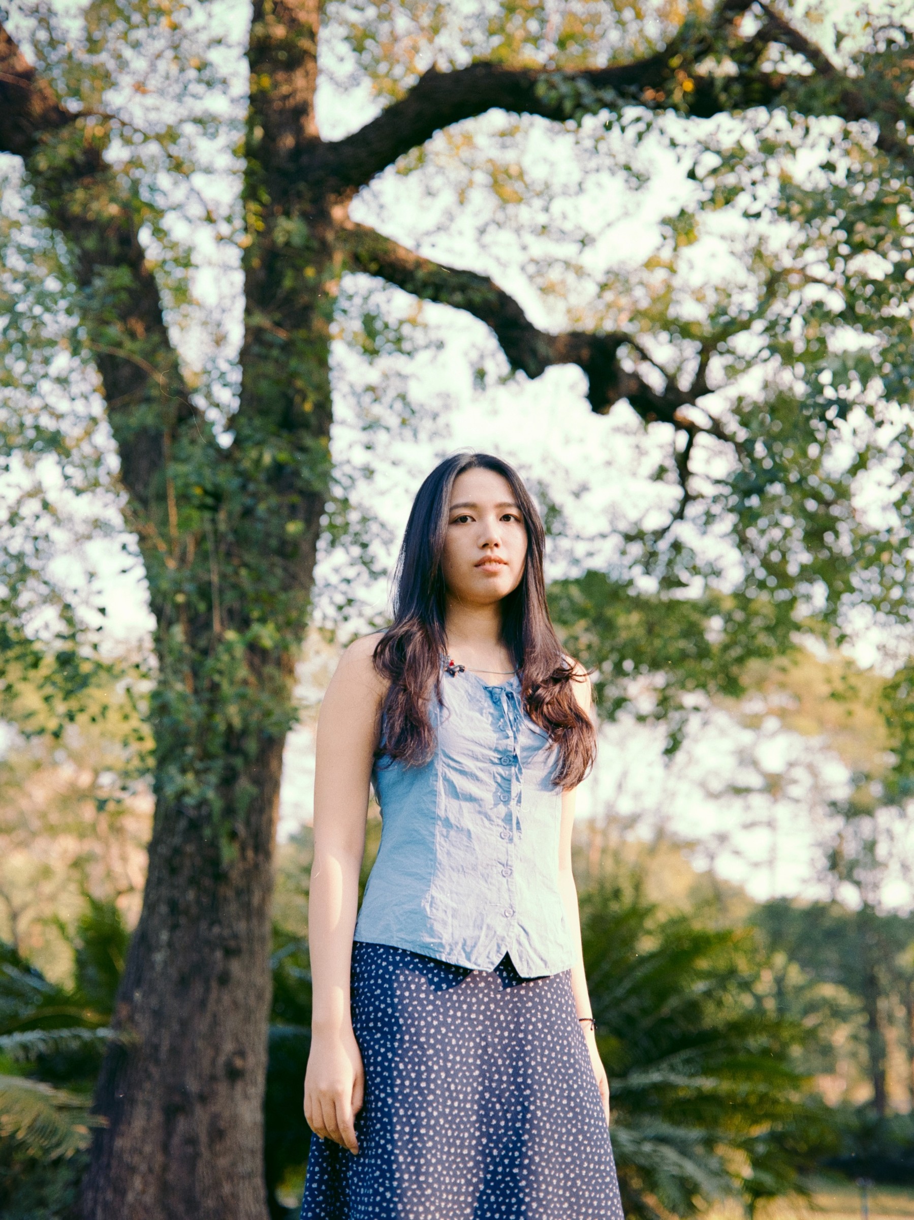 Woman in a blue top standing beneath a flowering tree
