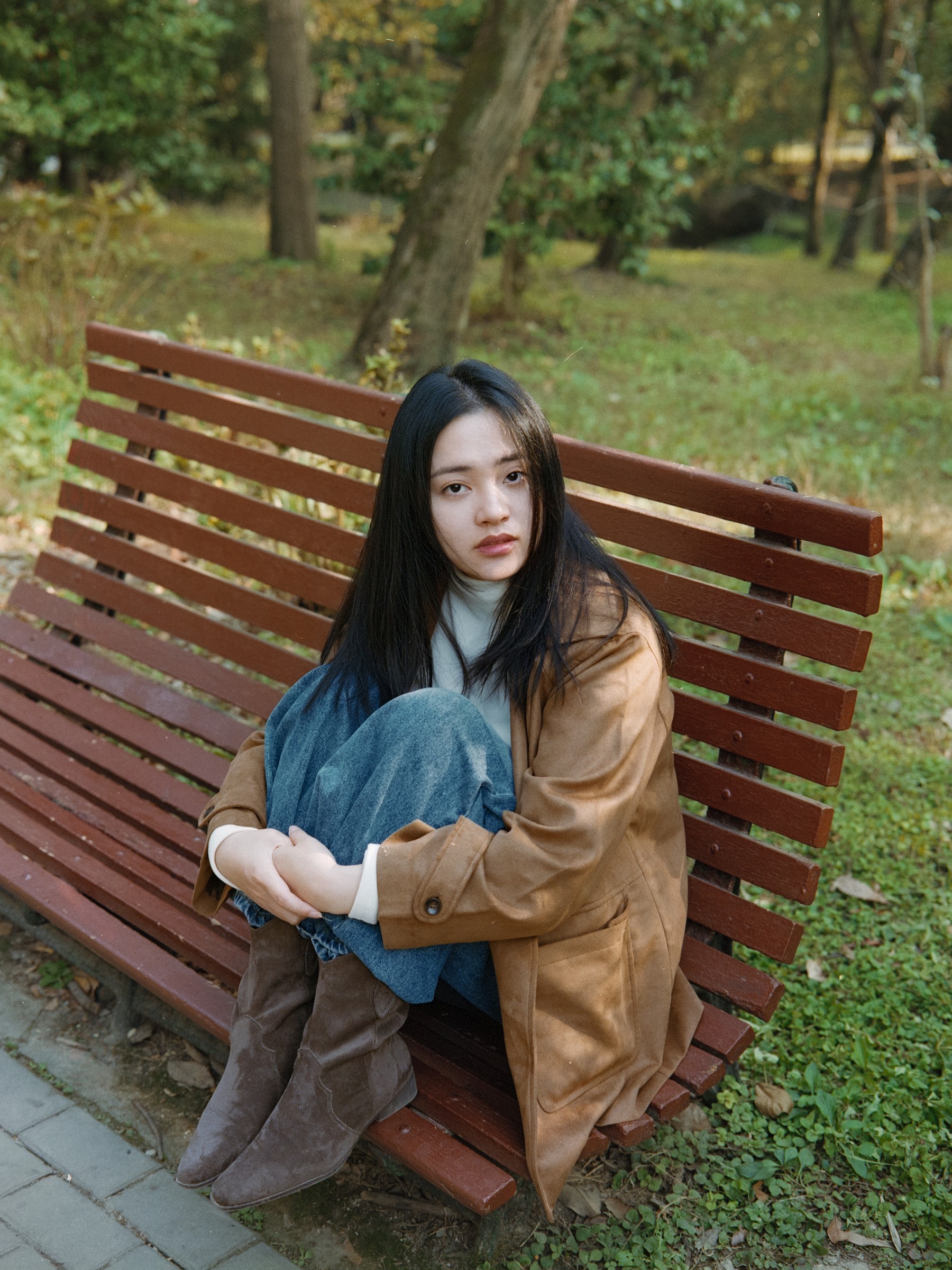 Woman in a brown jacket seated on a wooden park bench