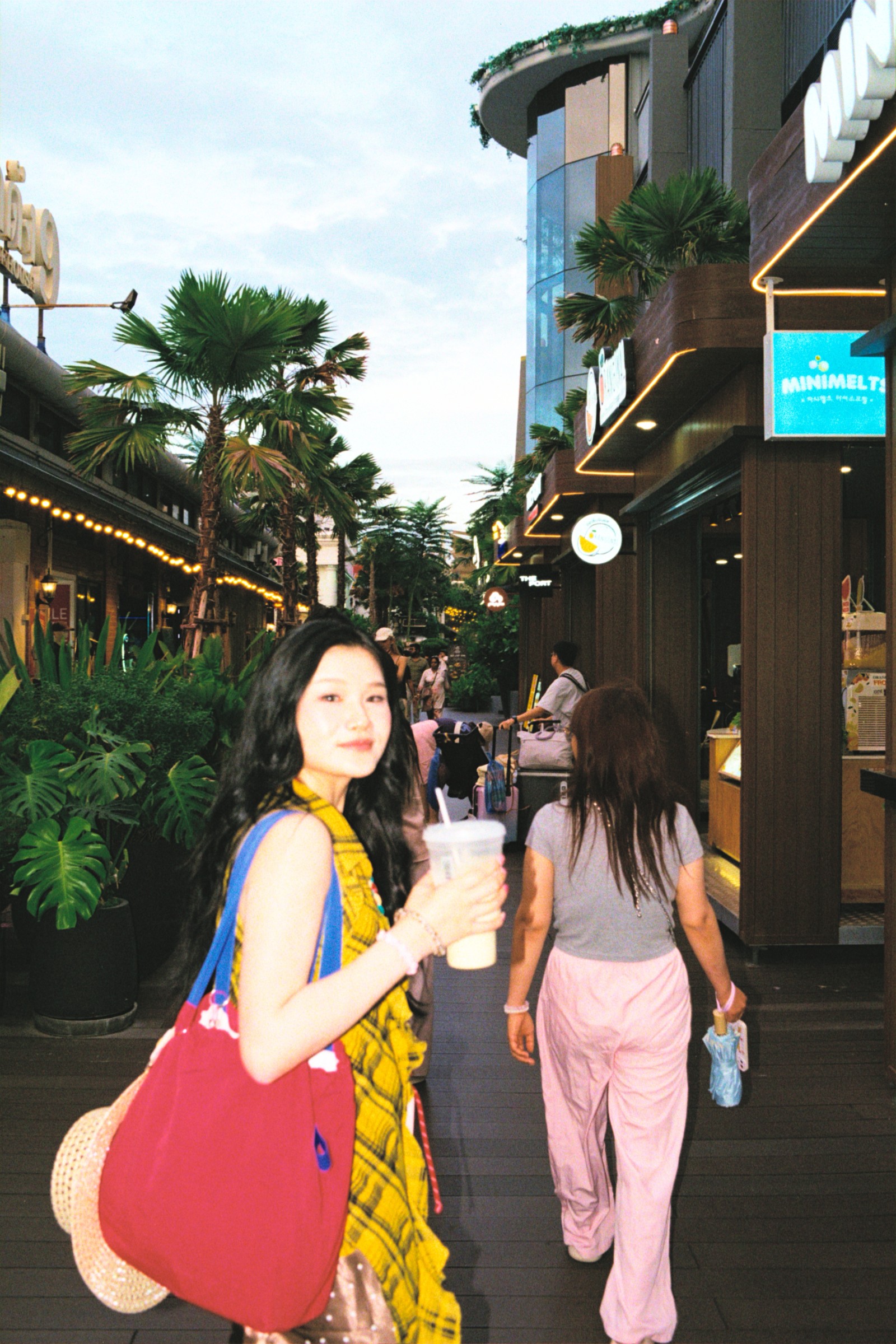 Woman in a yellow dress holding a drink on a tropical street