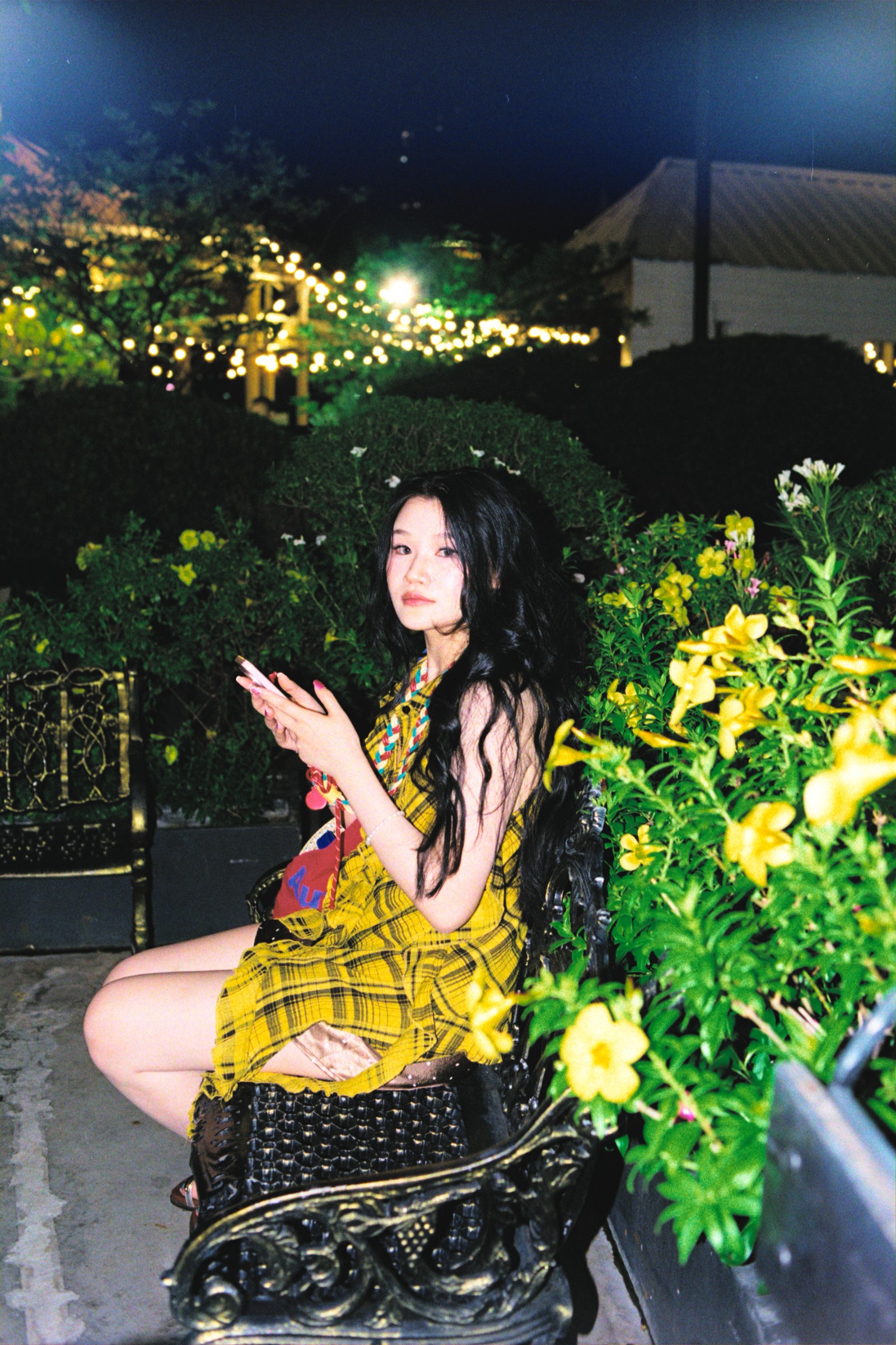 Woman in a yellow dress seated among illuminated flowers